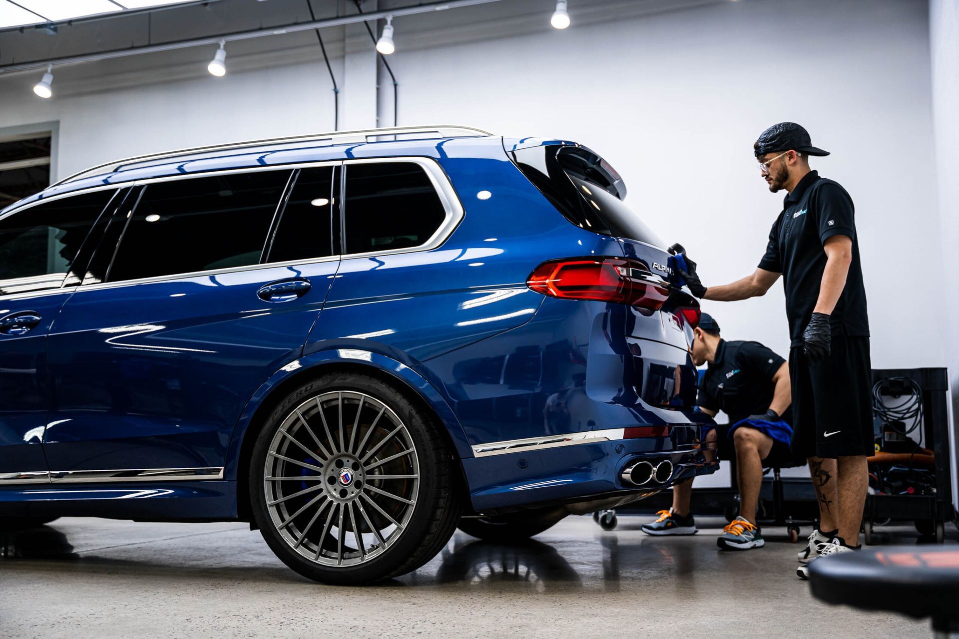 Two men are working on a blue car in a garage.