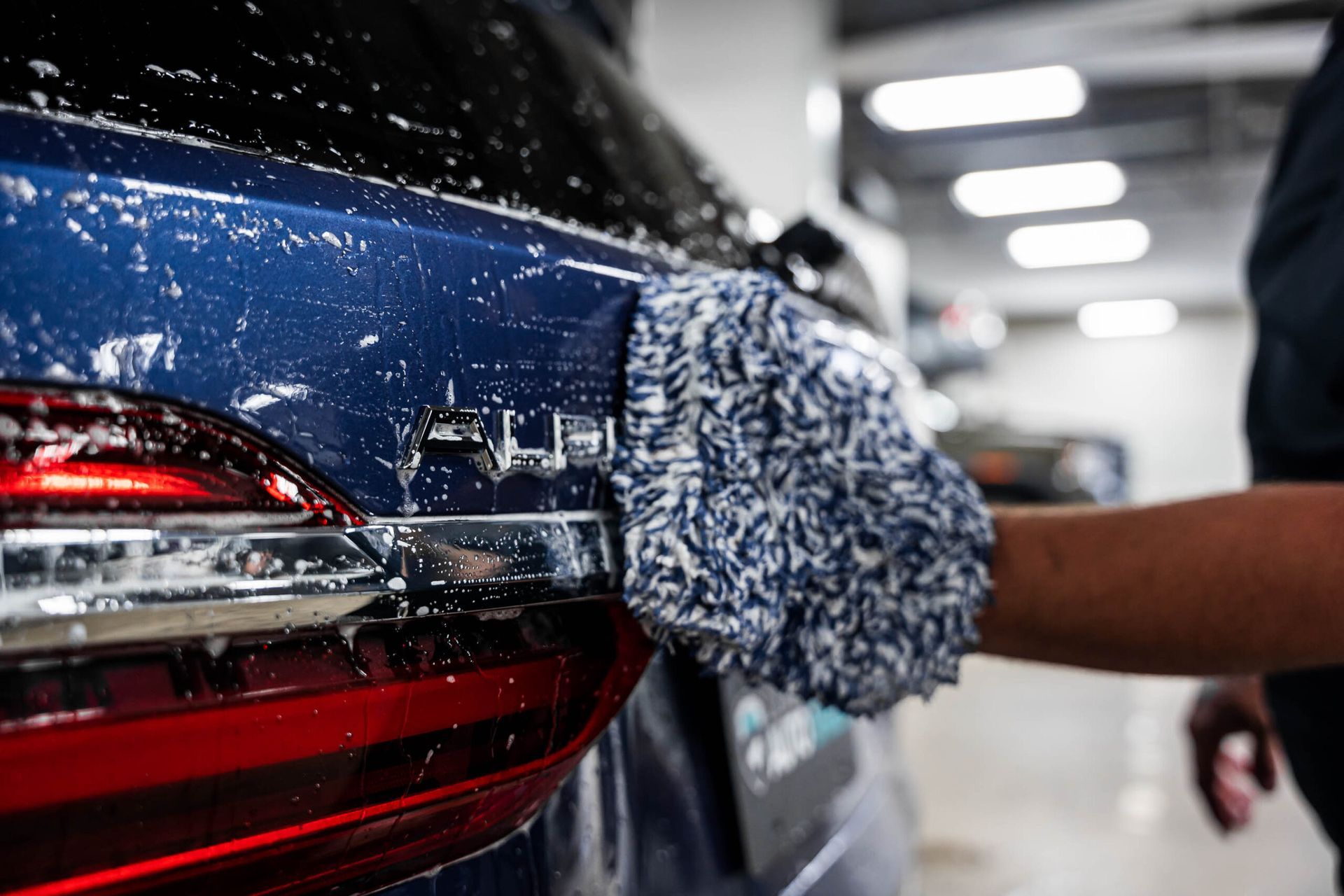 A person is washing a blue car with a glove.