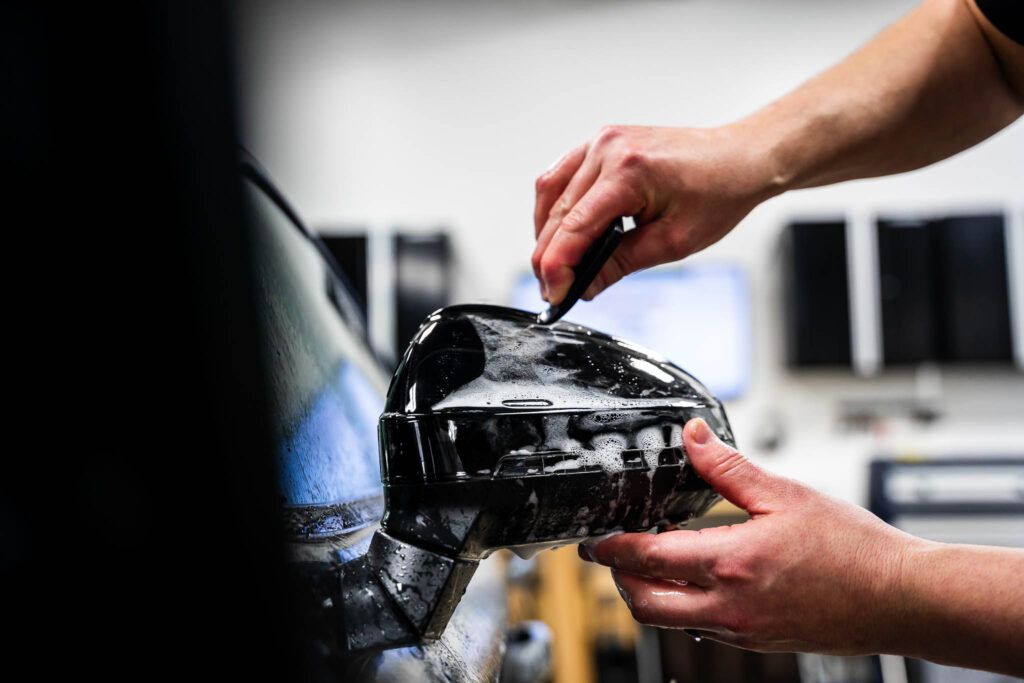 A person is cleaning a car side mirror with a brush.