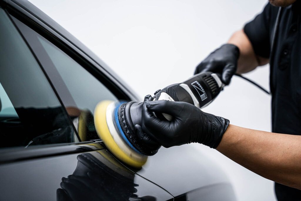 A man wearing black gloves is polishing a car with a machine.