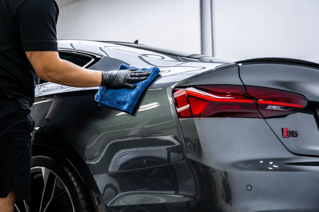 A man is cleaning a car with a blue cloth.