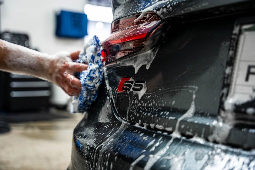 A person is washing a black car with a cloth.