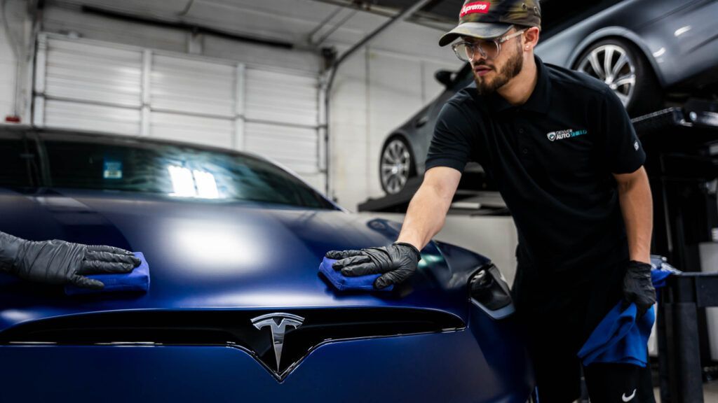 A man is cleaning the hood of a tesla model s in a garage.