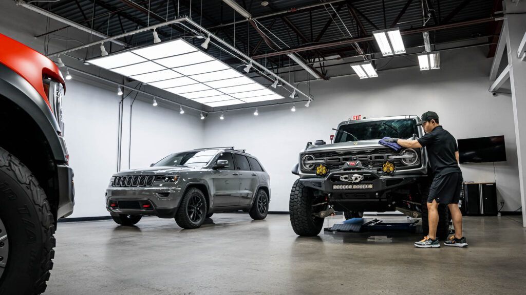 A man is cleaning the windshield of a jeep in a garage.