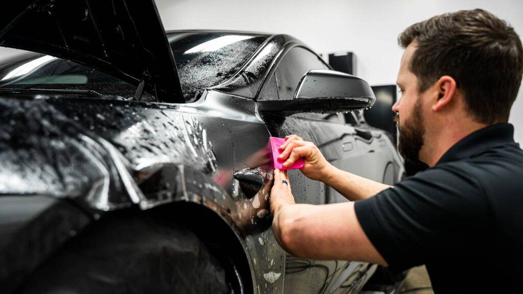 A man is wrapping a black car with a pink cloth.