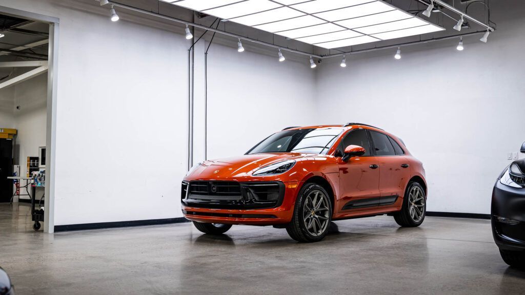 An orange porsche macan turbo is parked in a garage.