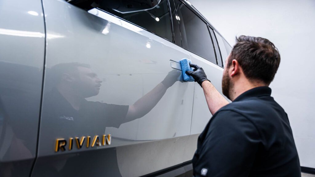 A man is cleaning the side of a silver suv with a cloth.