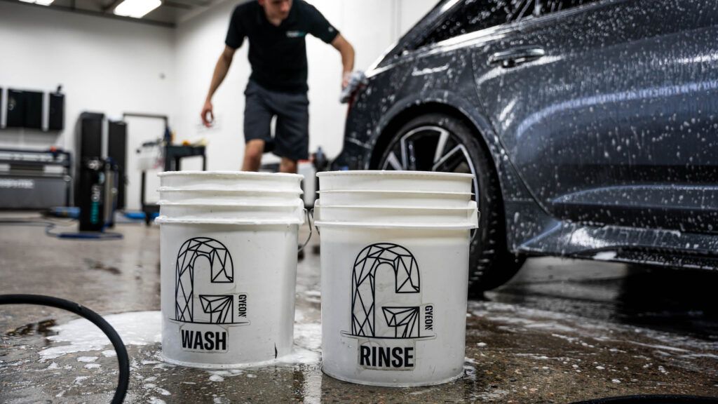 A man is washing a car in a garage with two buckets.