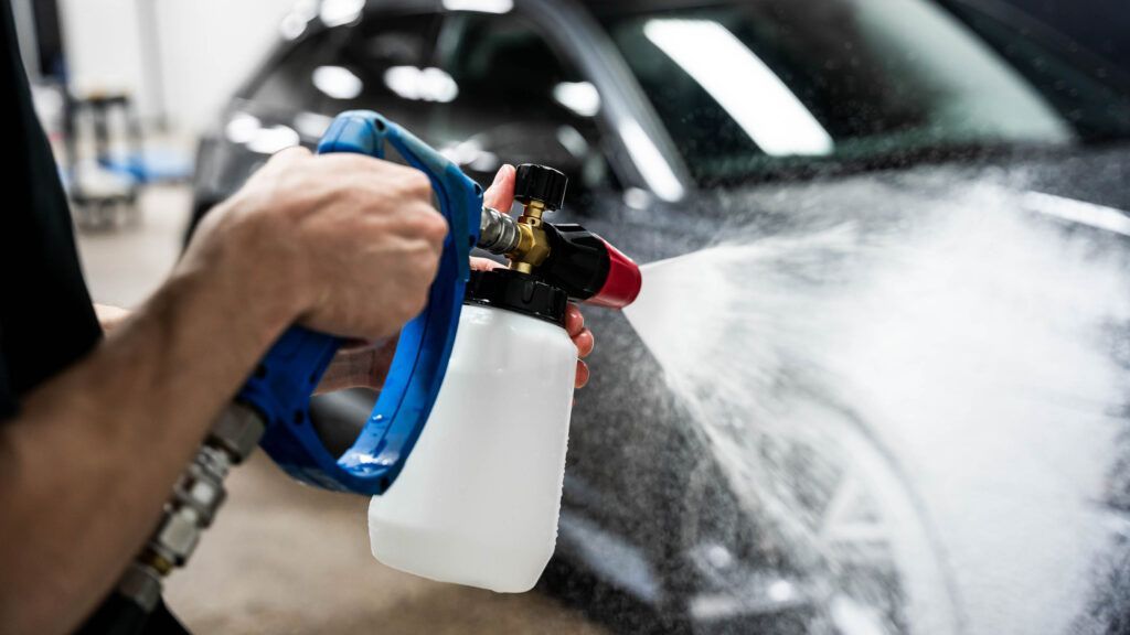 A person is spraying water on a car with a spray bottle.