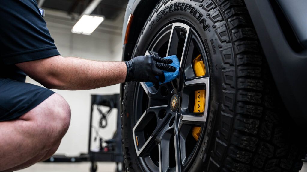 A man is cleaning the wheels of a car with a cloth.