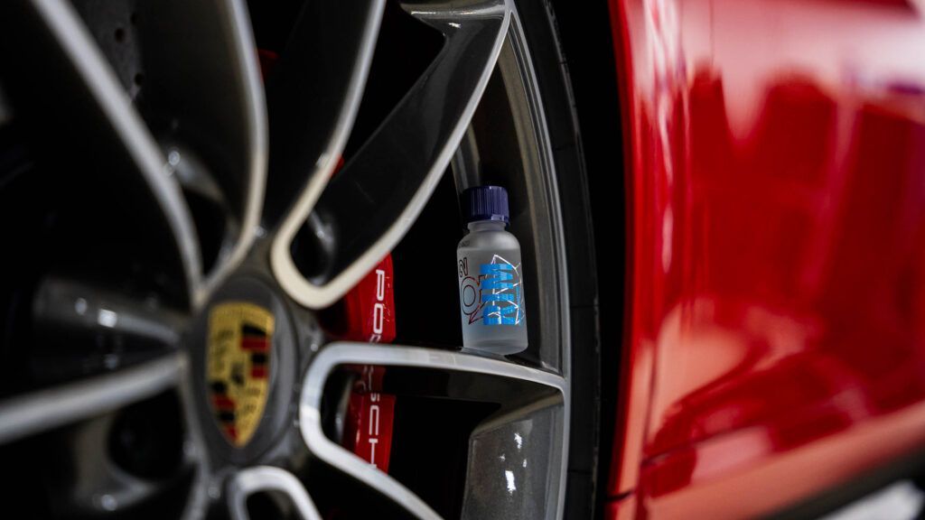 A close up of a red car wheel with a bottle of liquid on it.