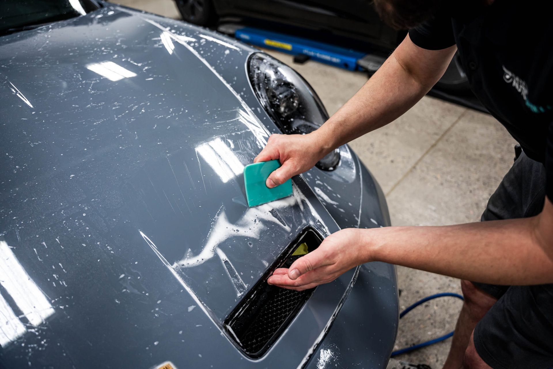 A man is cleaning the hood of a car with a sponge.