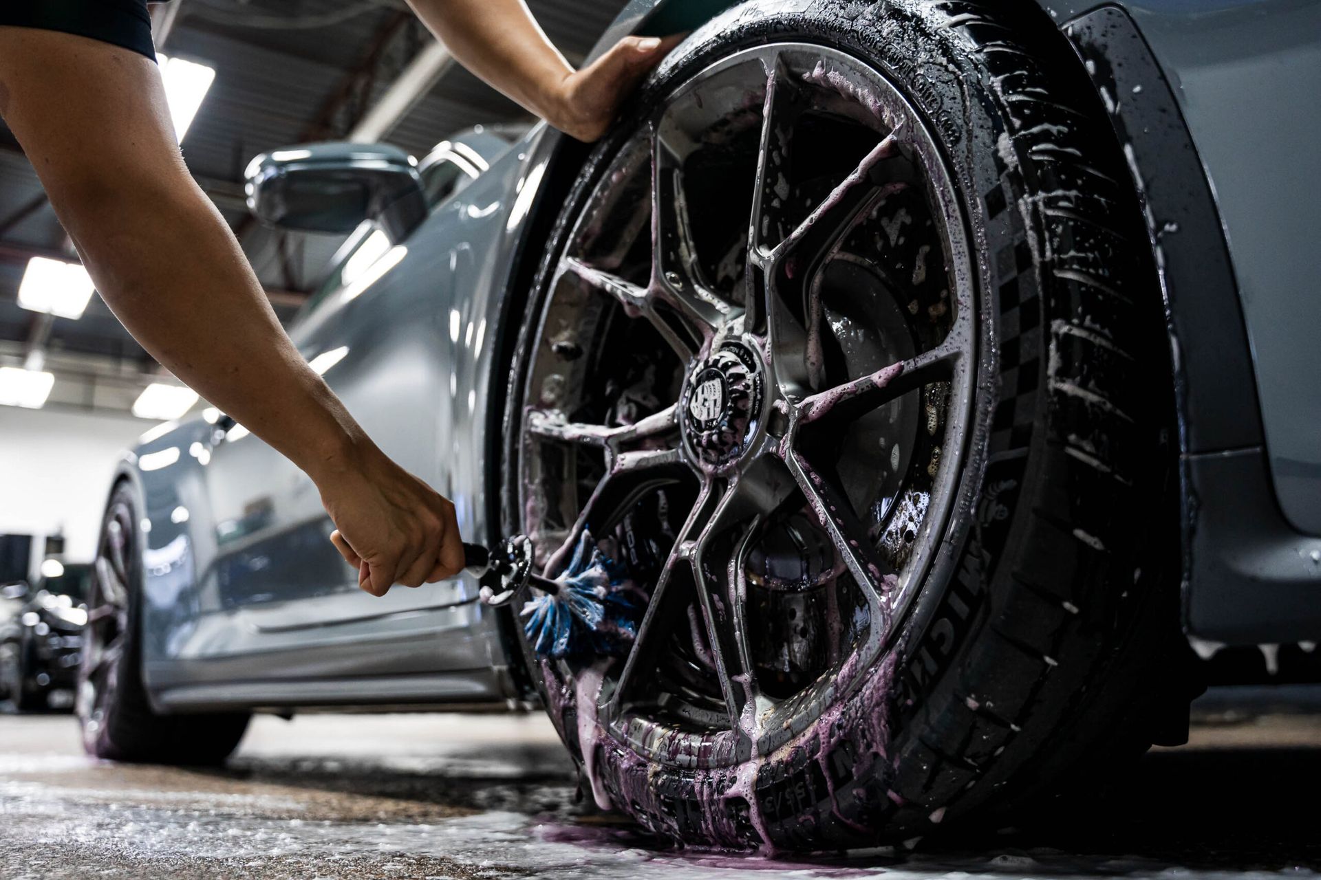 A person is cleaning a car wheel with a brush.