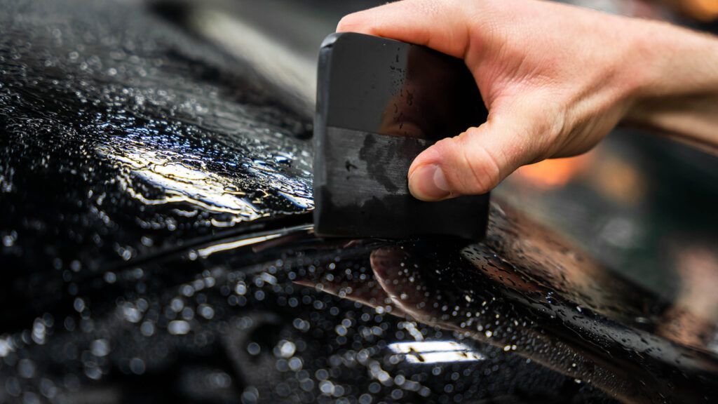 A person is applying tinted glass to a car with a spatula.