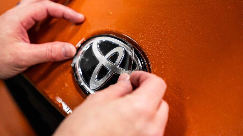 A person is peeling off a toyota logo from a car.