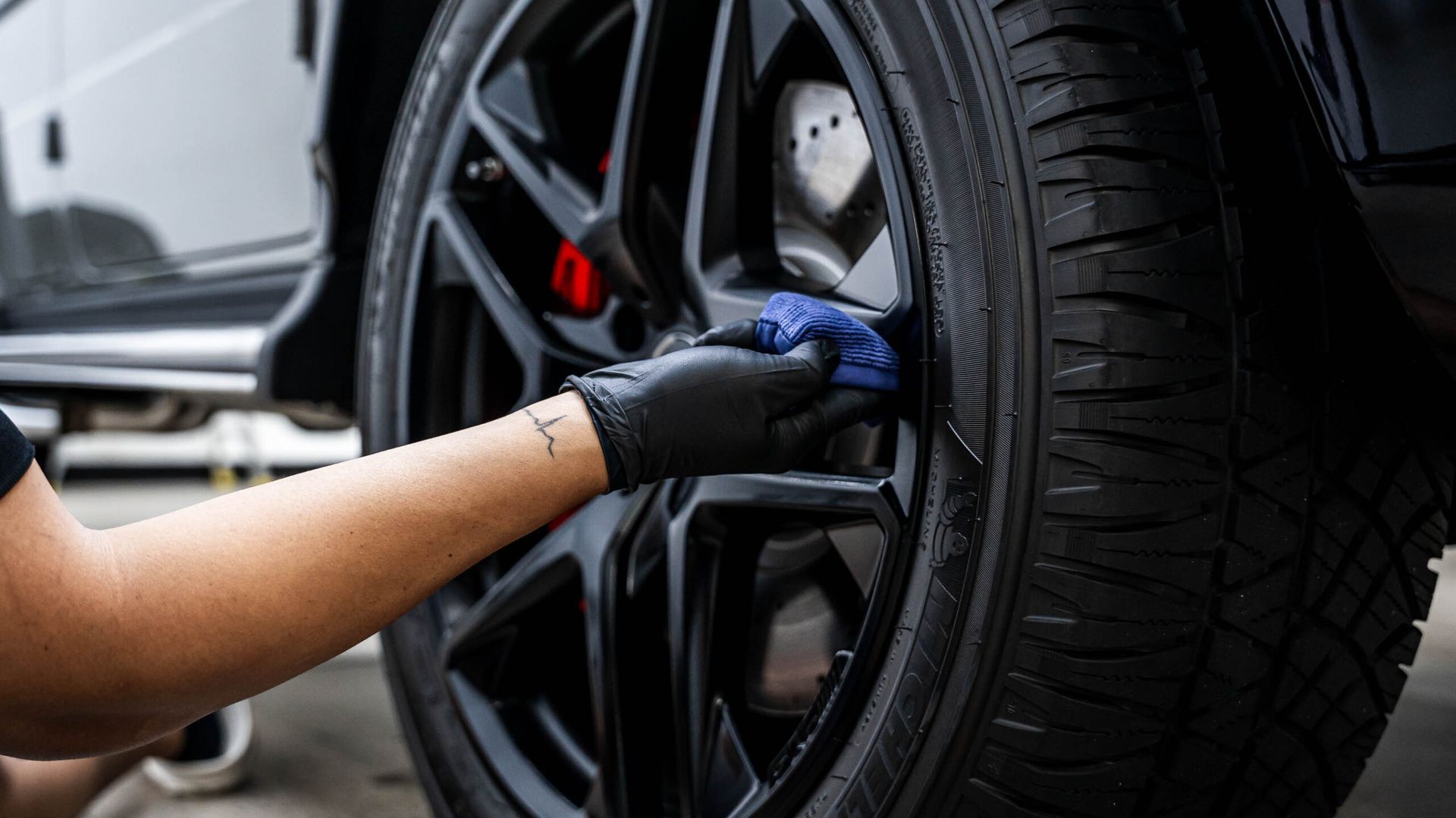 A person is cleaning a car wheel with a cloth.