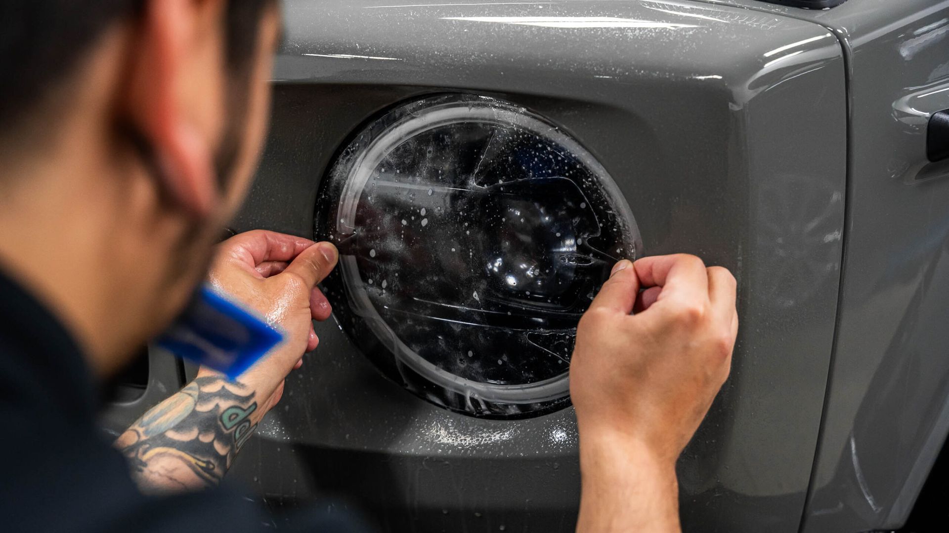 A man is applying a protective film to the headlights of a car.