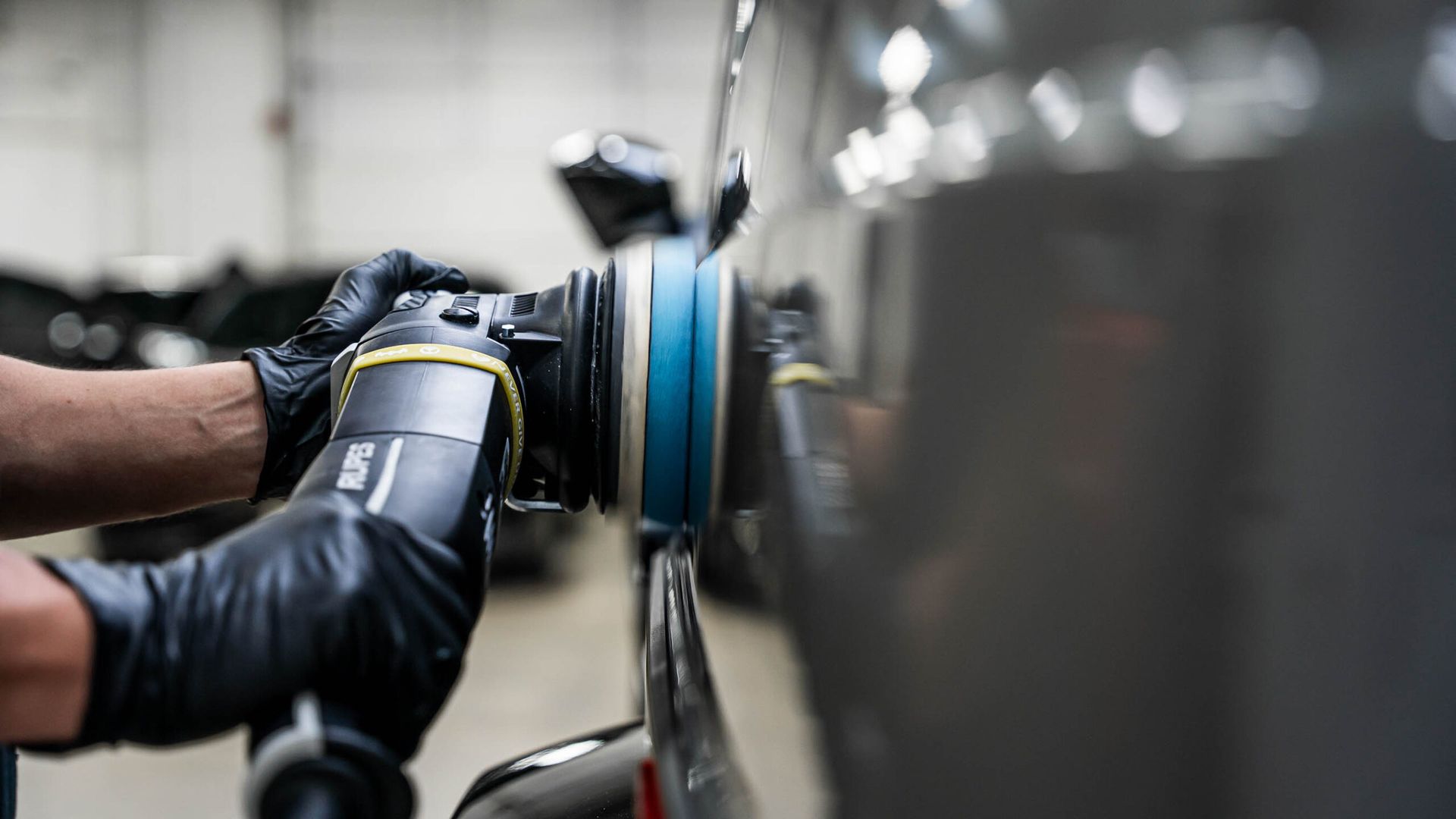 A person is polishing a car with a machine in a garage.