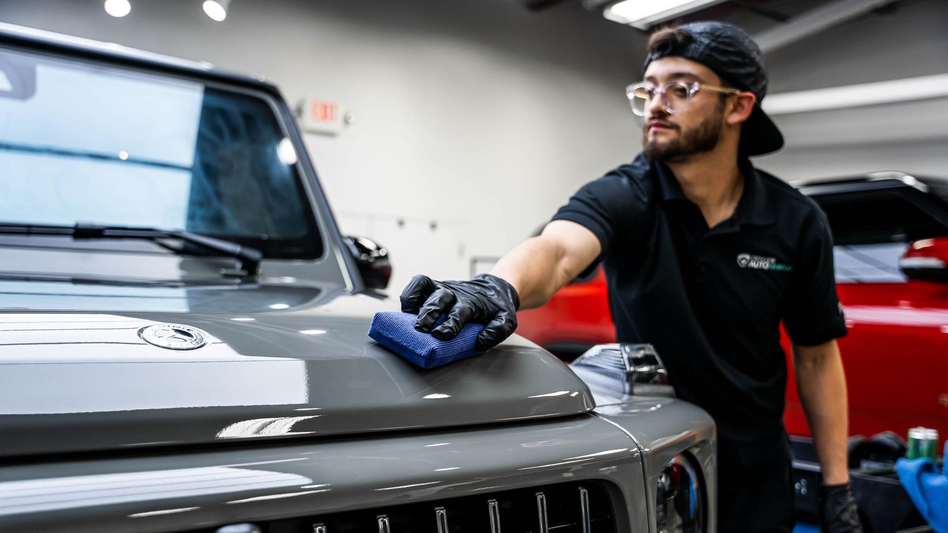 A man is cleaning the hood of a jeep with a cloth.