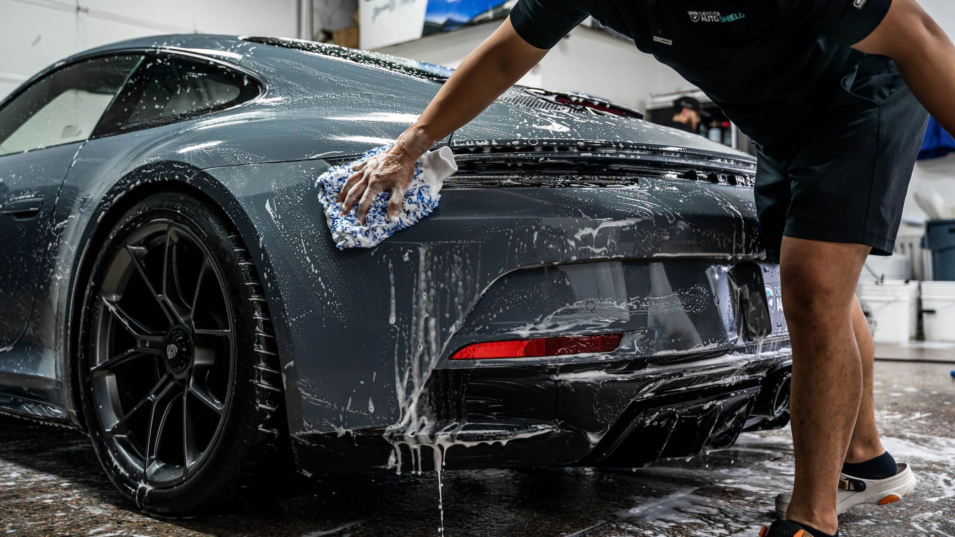 A man is washing a sports car with a towel in a garage.