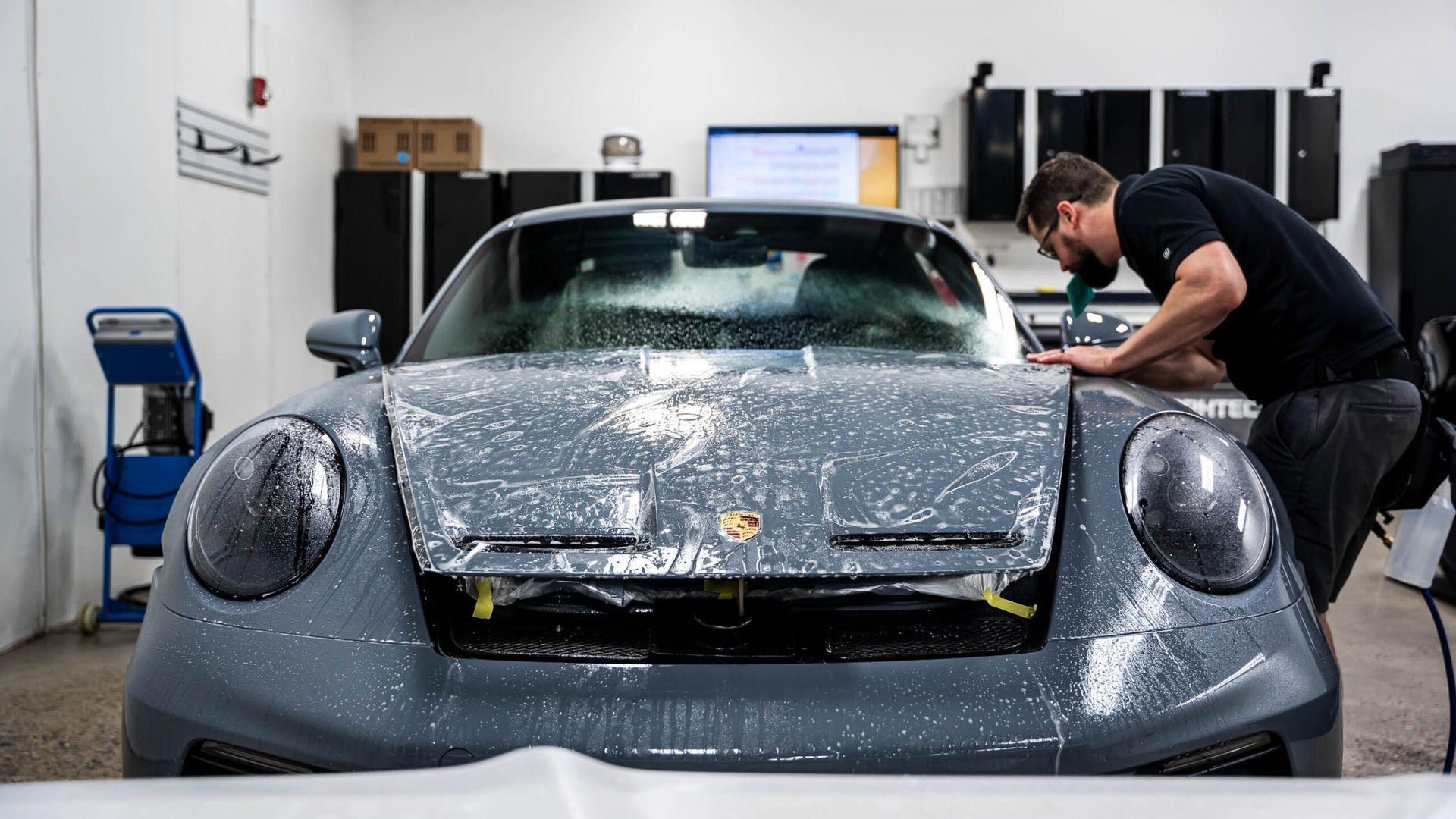 A man is wrapping a car with a protective film in a garage.