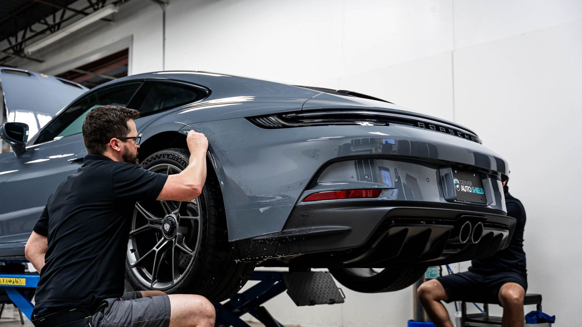 A man is working on a car on a lift in a garage.