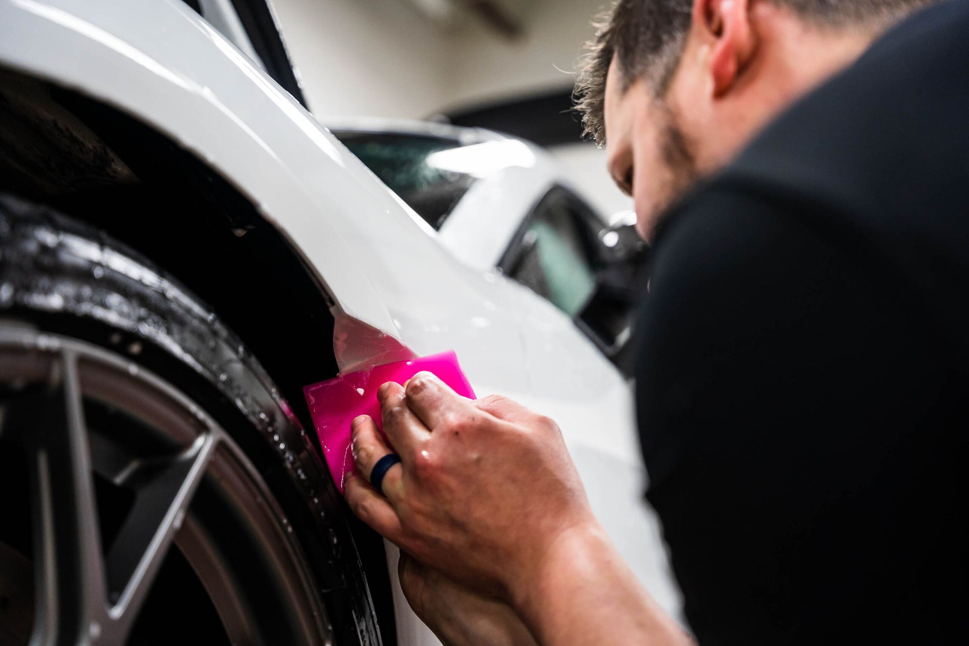 A man is cleaning a white car with a pink sponge.