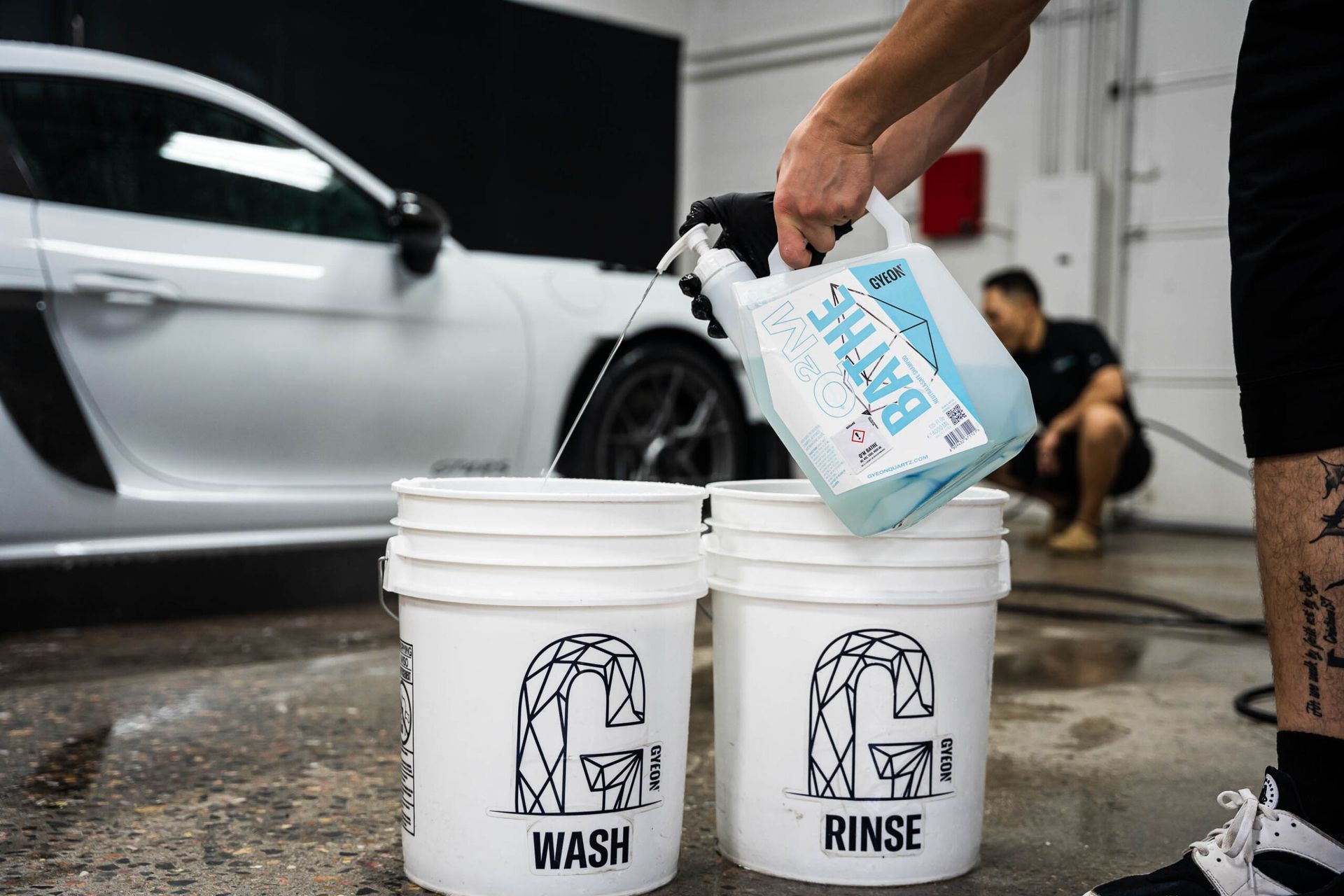 A person is pouring water into two buckets next to a car.