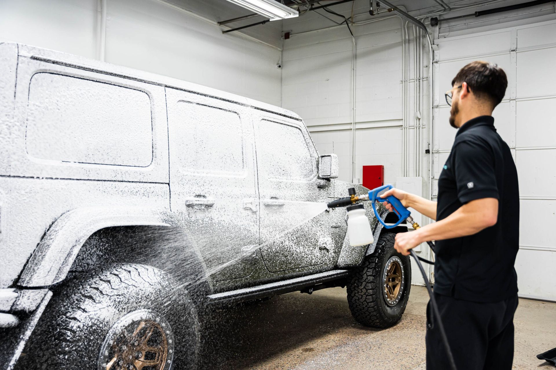 A man is washing a jeep with foam in a garage.