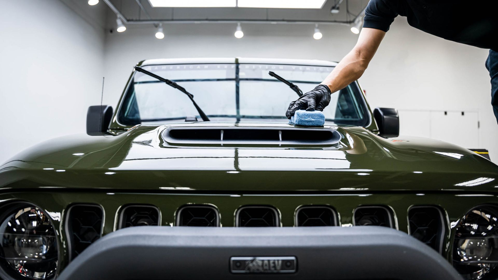 A man is polishing the hood of a jeep in a garage.