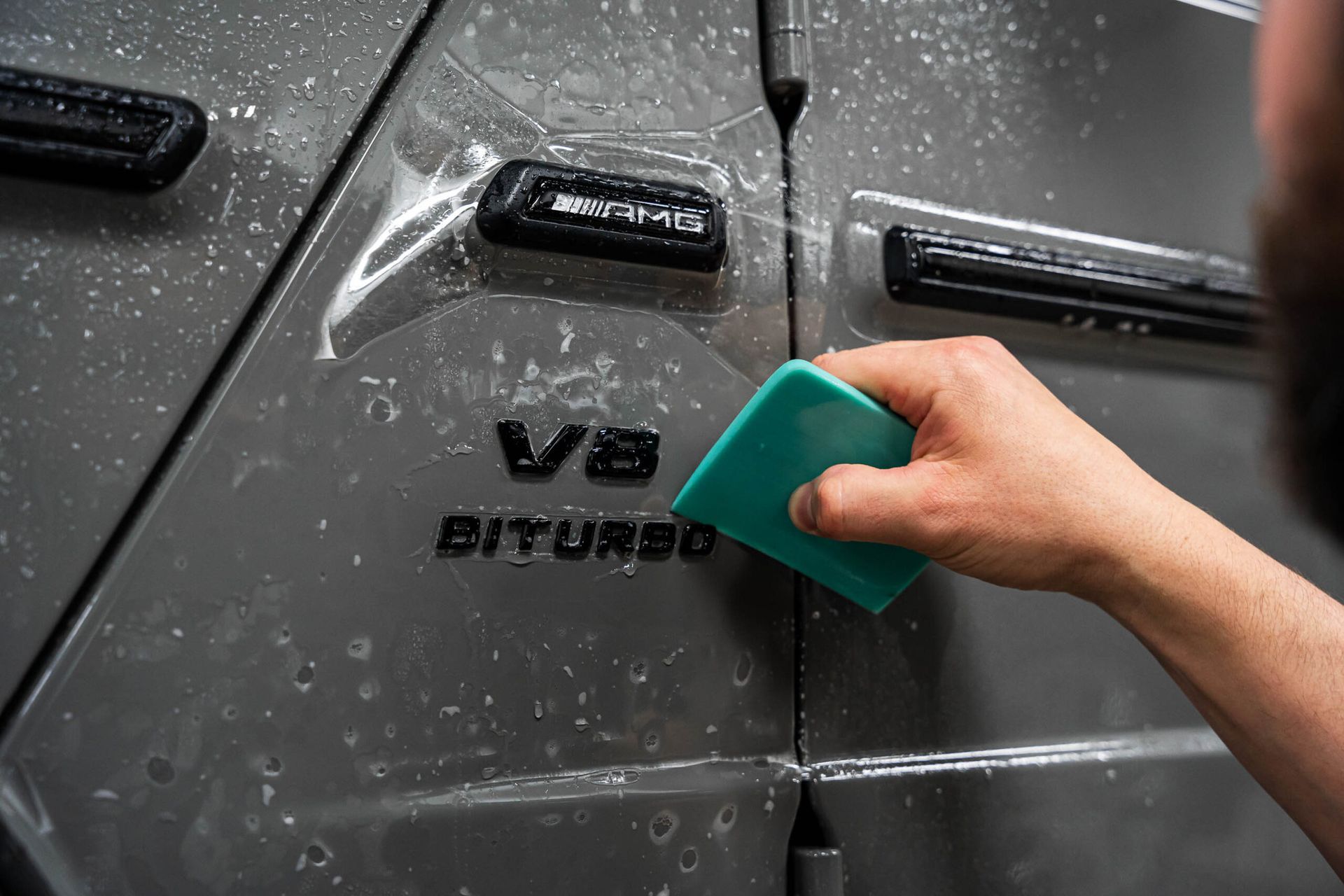 A person is applying protective film to the side of a car.