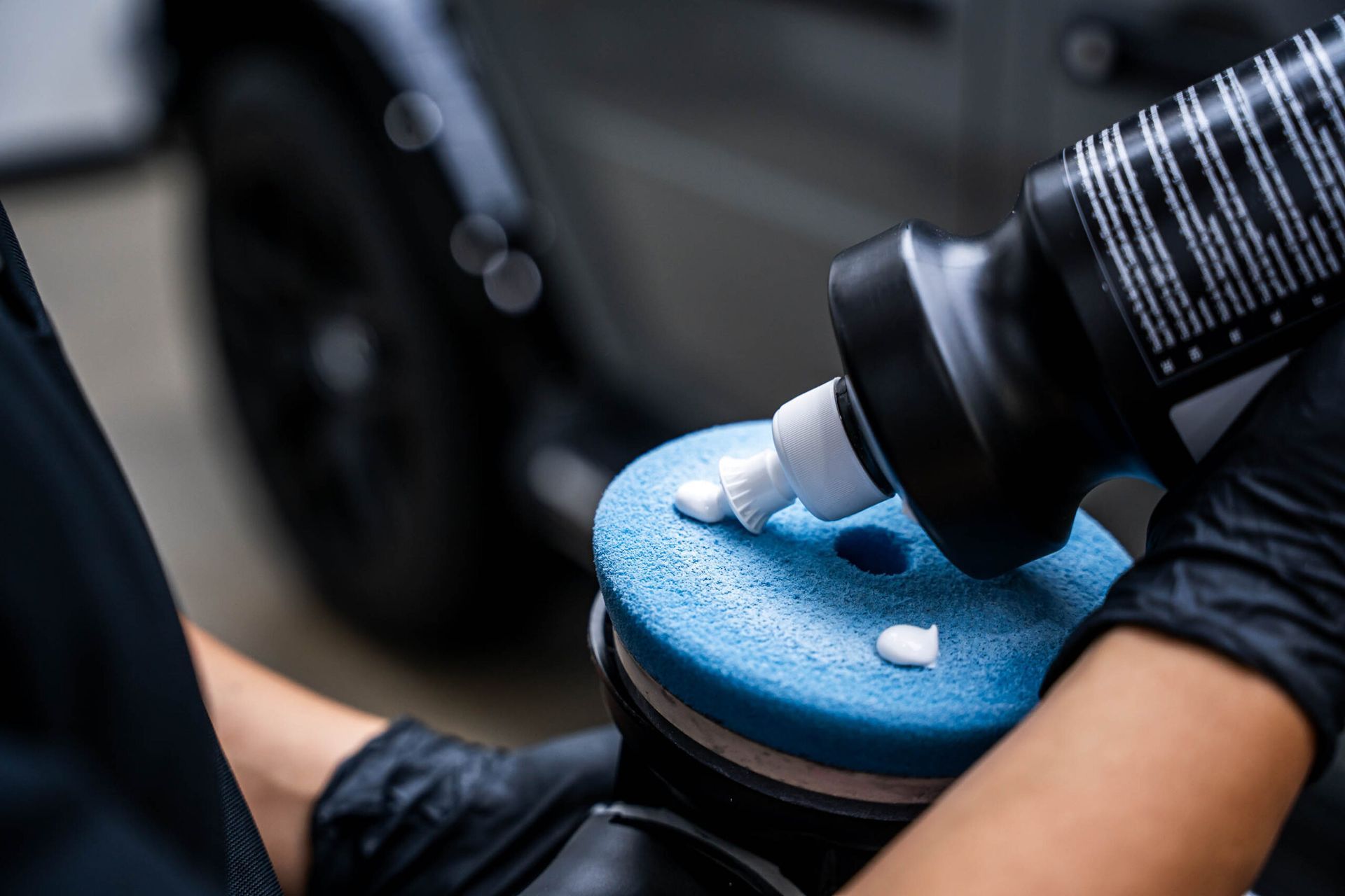 A person is polishing a car with a sponge and a bottle of polish.