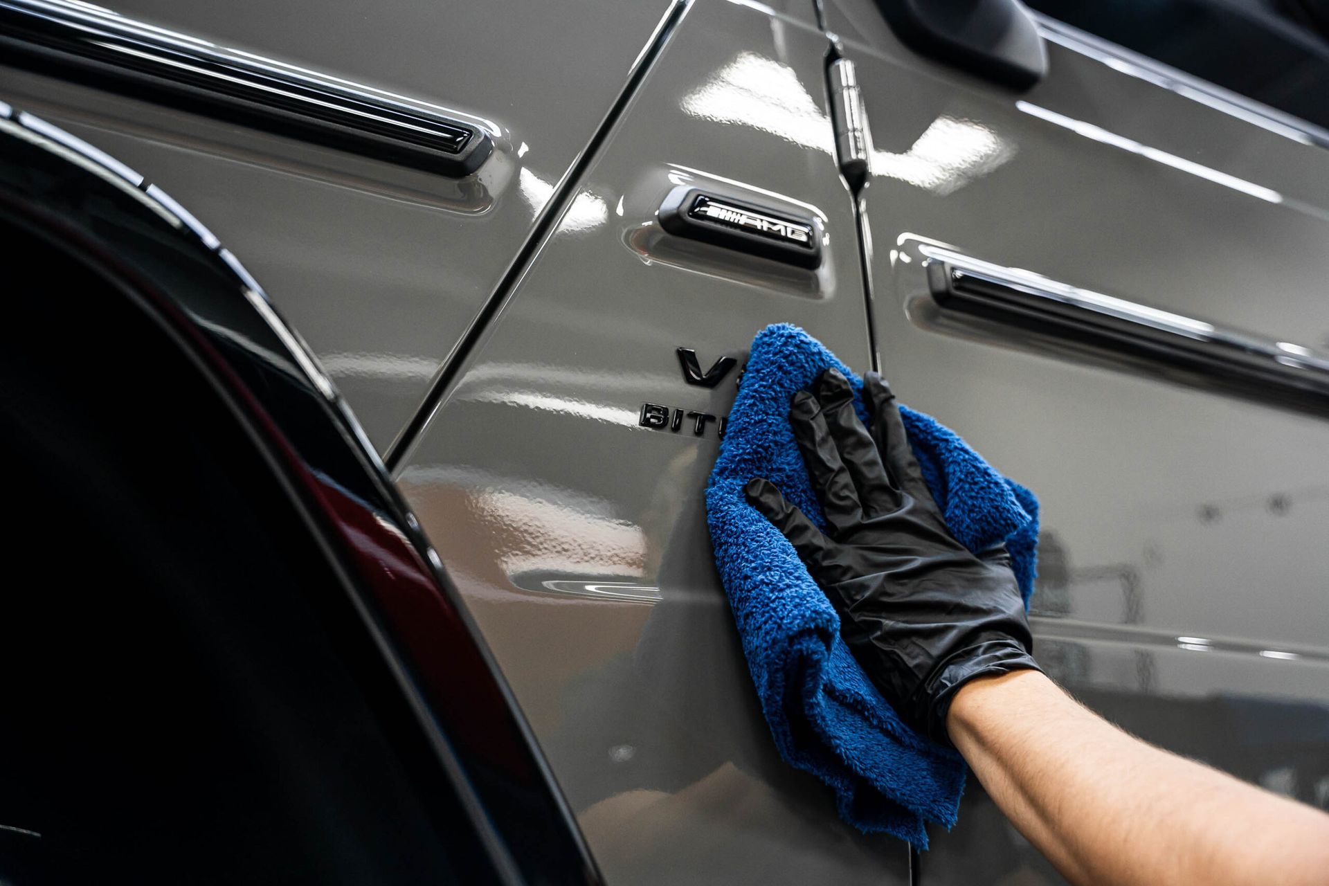 A person is cleaning a car with a blue cloth.