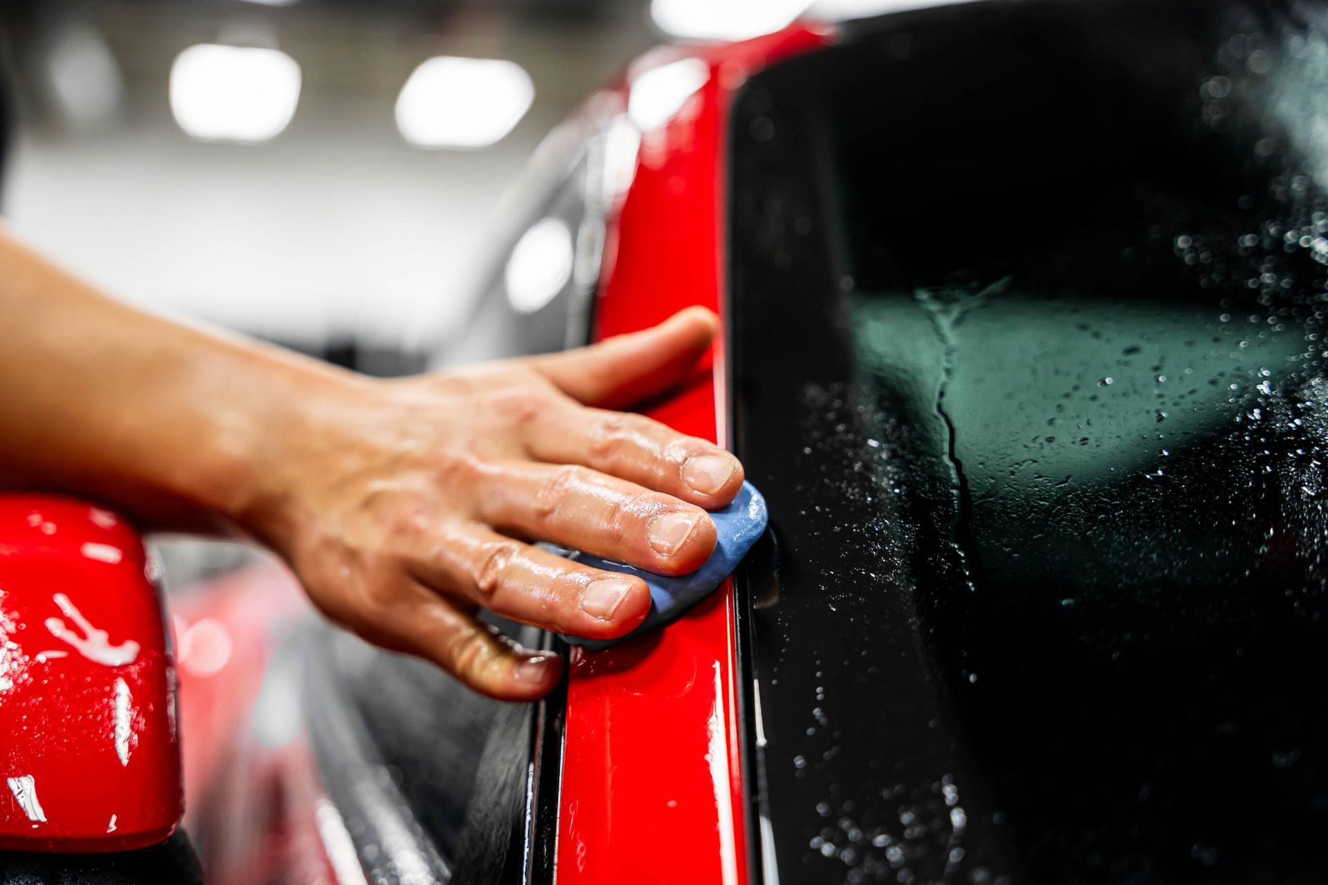 A person is cleaning a red car with a sponge.