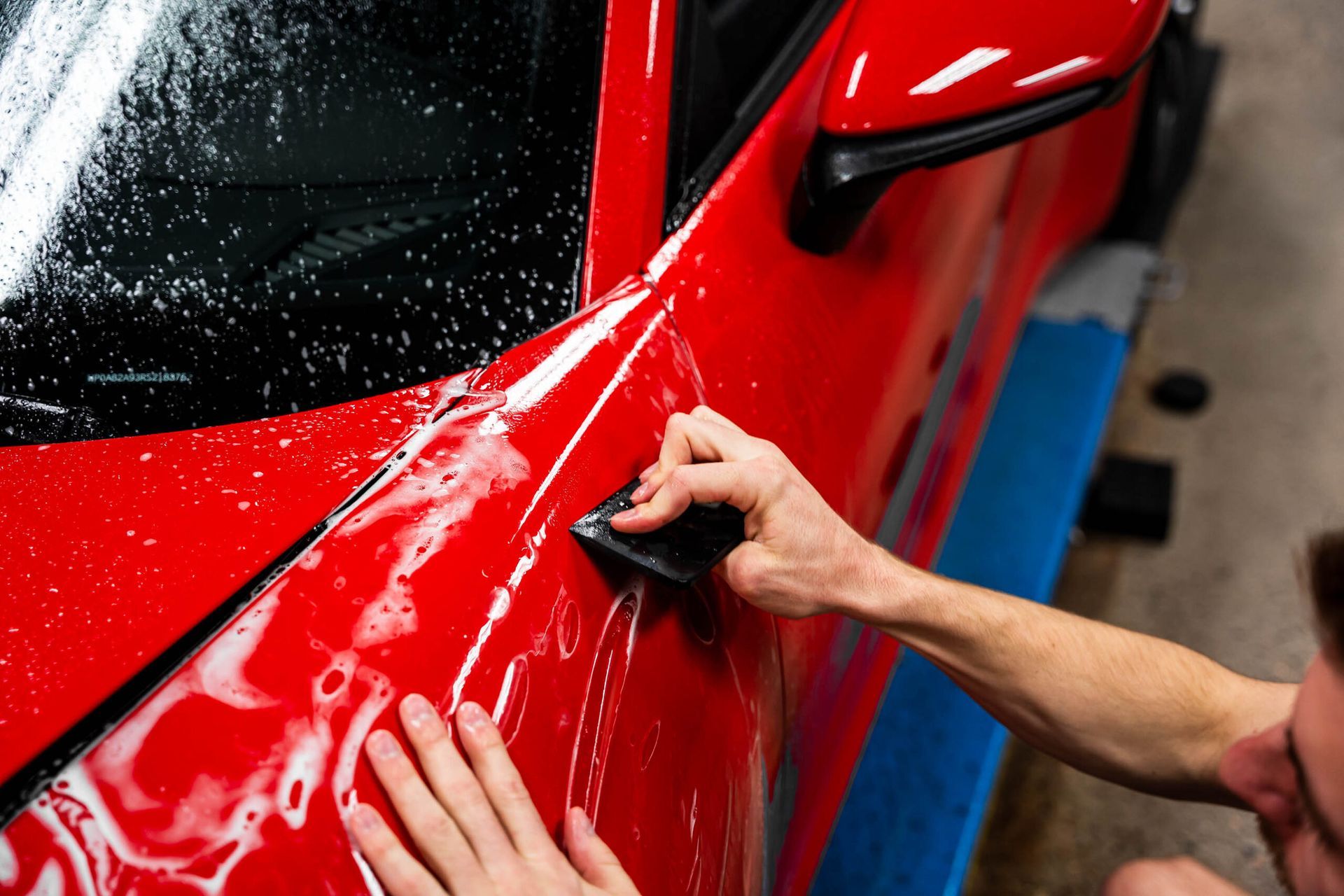 A person is applying a protective film to a red car.