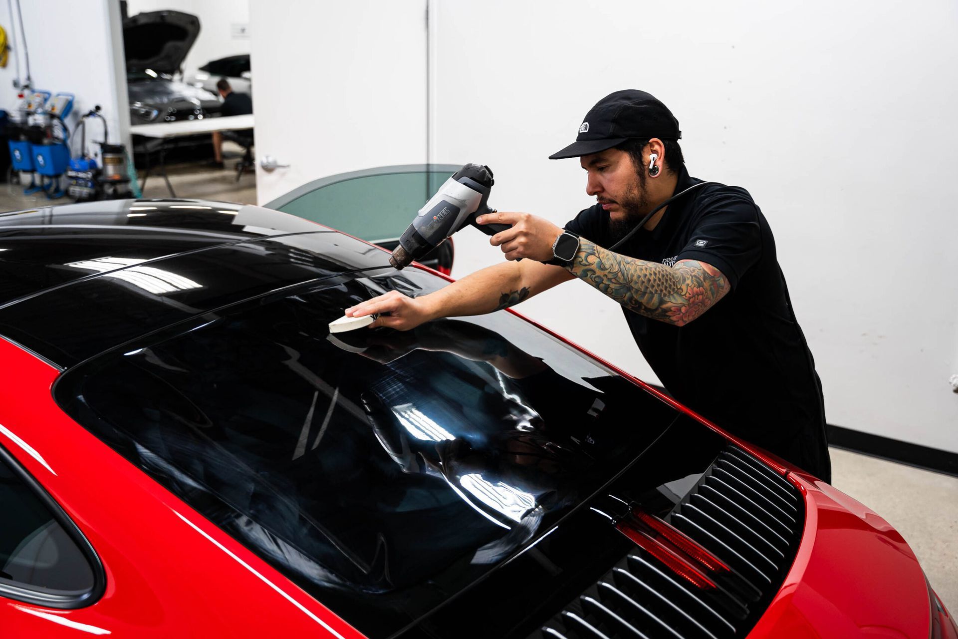 A man is wrapping the roof of a red car.