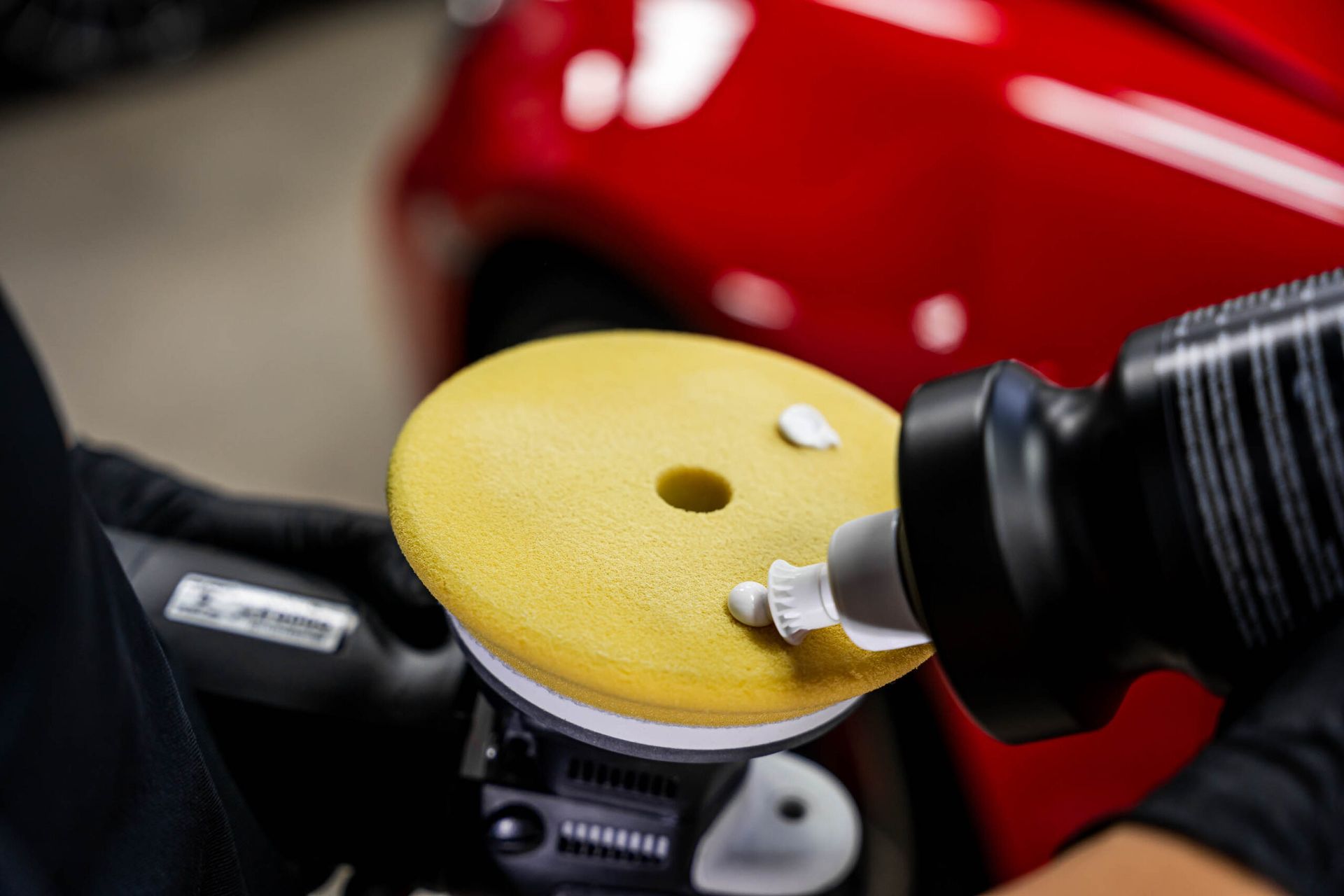 A person is polishing a red car with a yellow polishing pad.