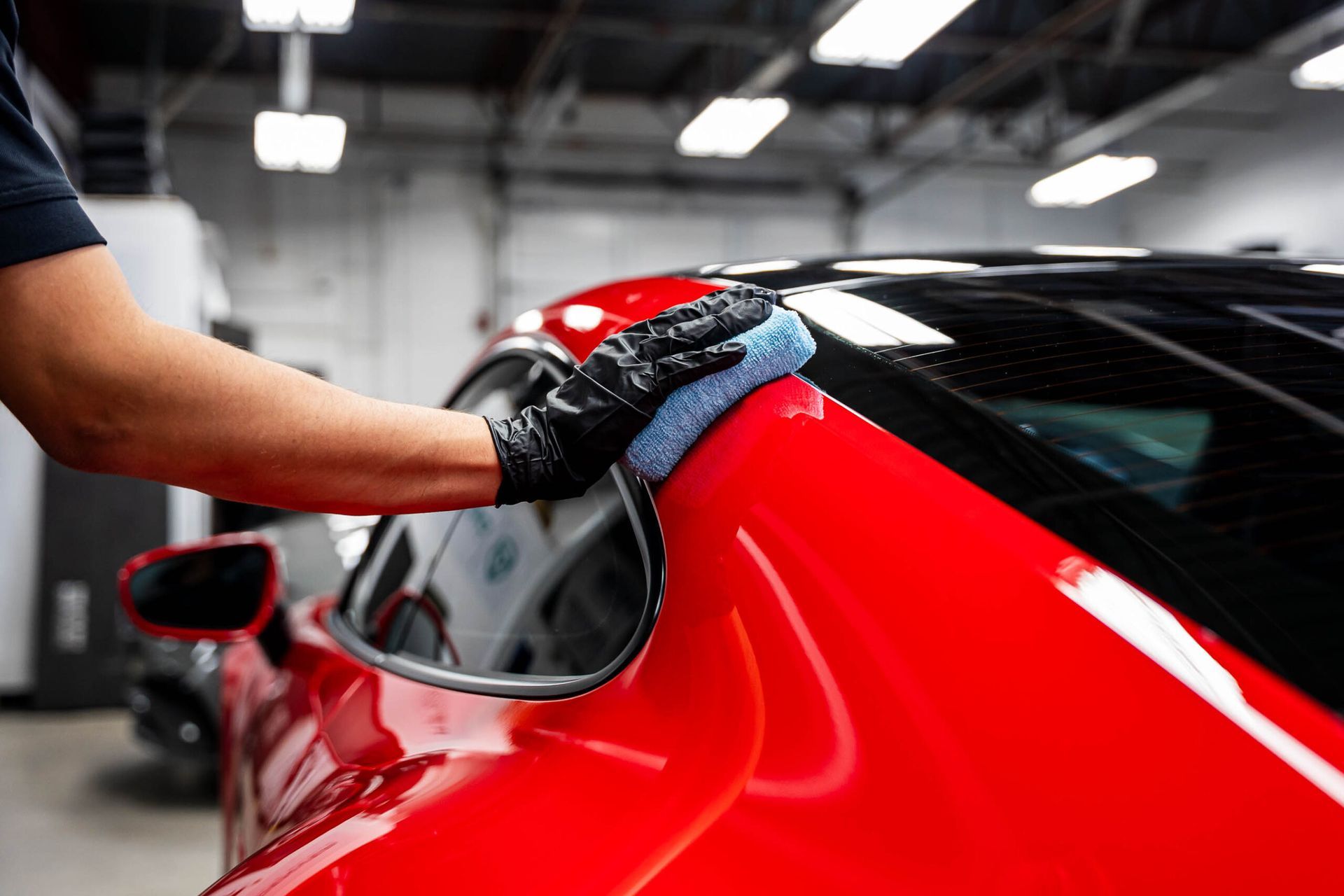 A man is cleaning a red car with a cloth in a garage.