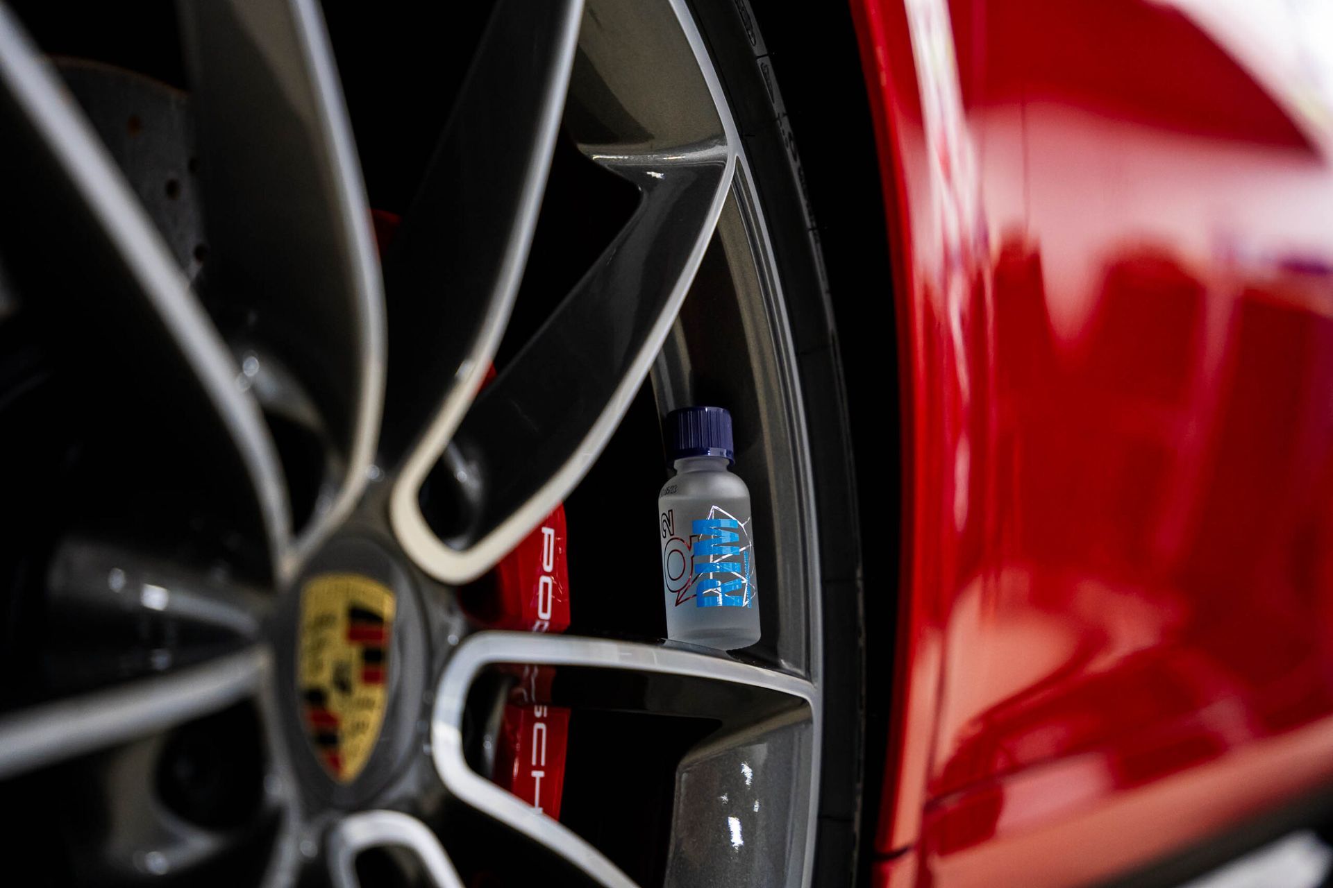 A close up of a red car wheel with a bottle of liquid on it.