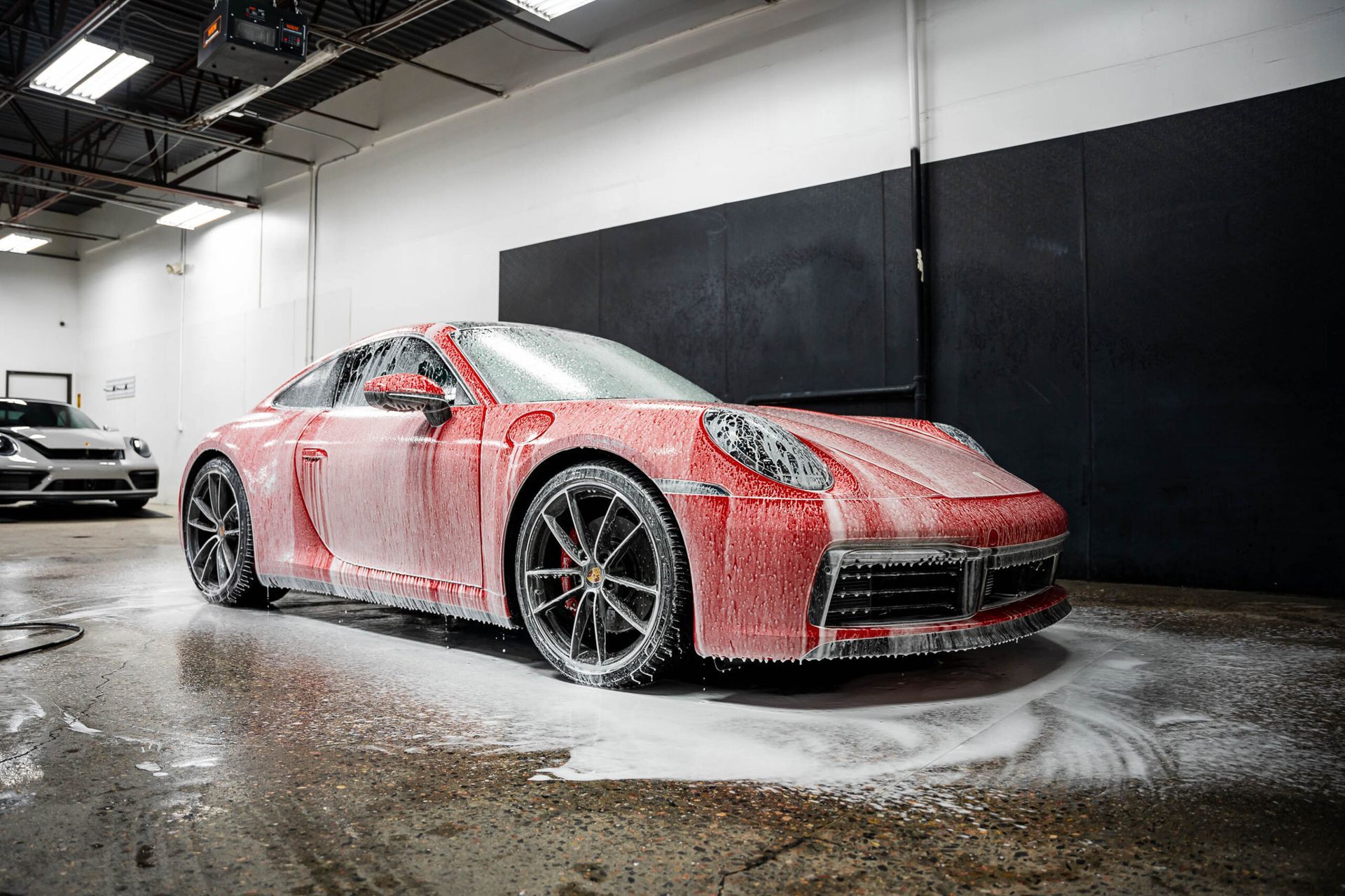 A red porsche 911 is covered in foam in a garage.