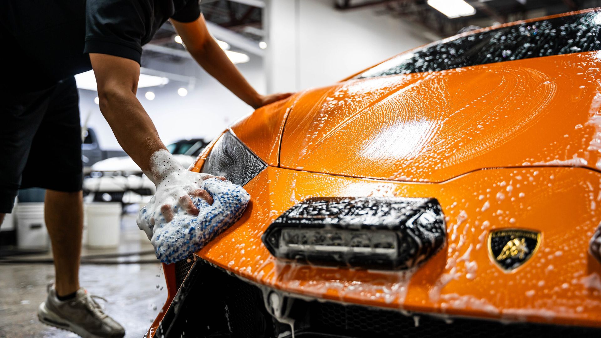 A man is washing an orange lamborghini with a sponge.