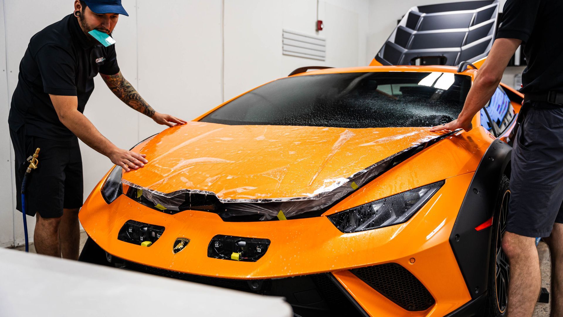 Two men are wrapping an orange sports car with a protective film.