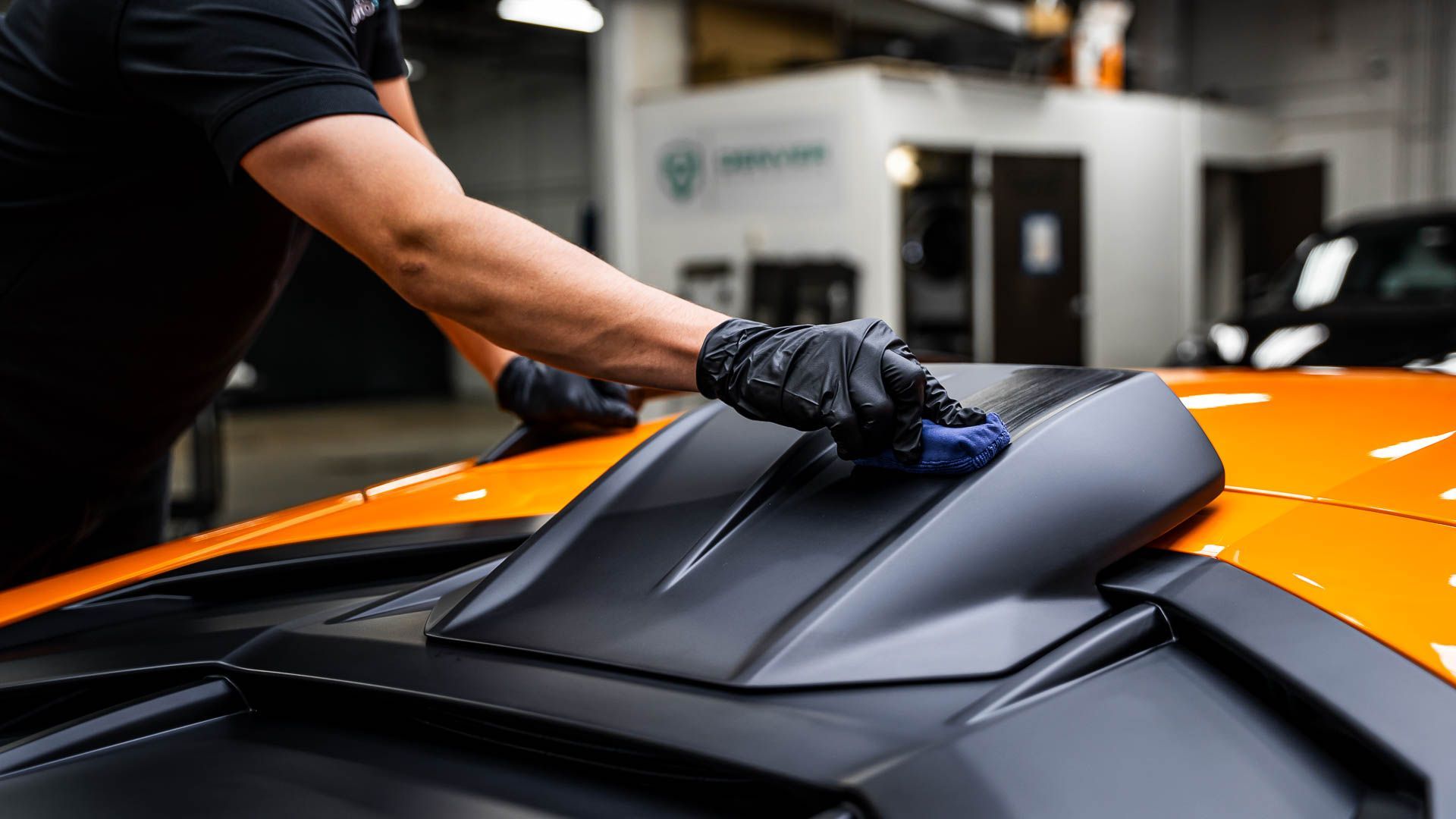 A man is cleaning the hood of an orange sports car.