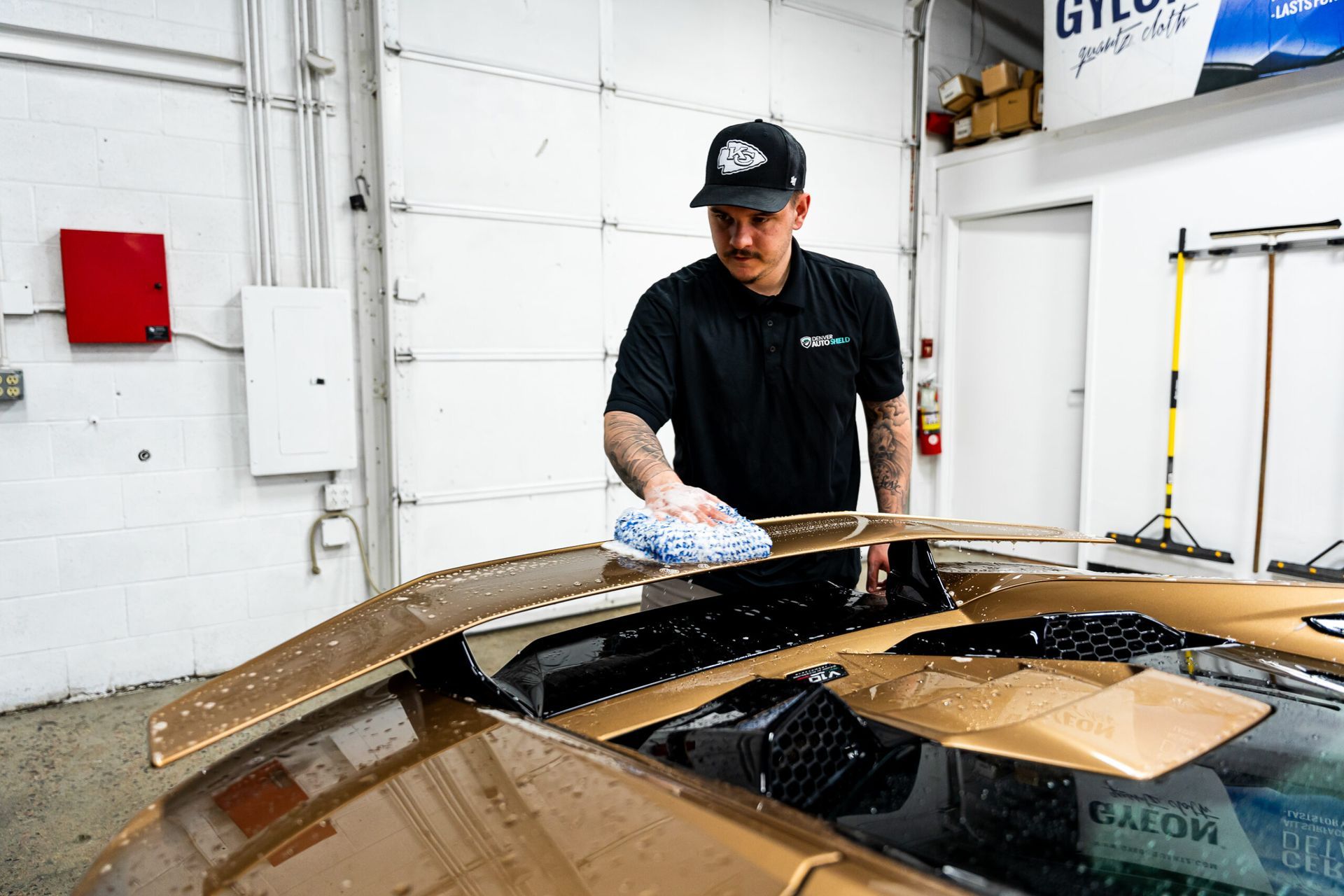 A man is cleaning the hood of a car in a garage.