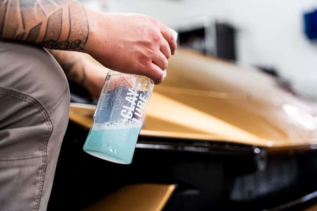 A person is holding a bottle of liquid in front of a car.