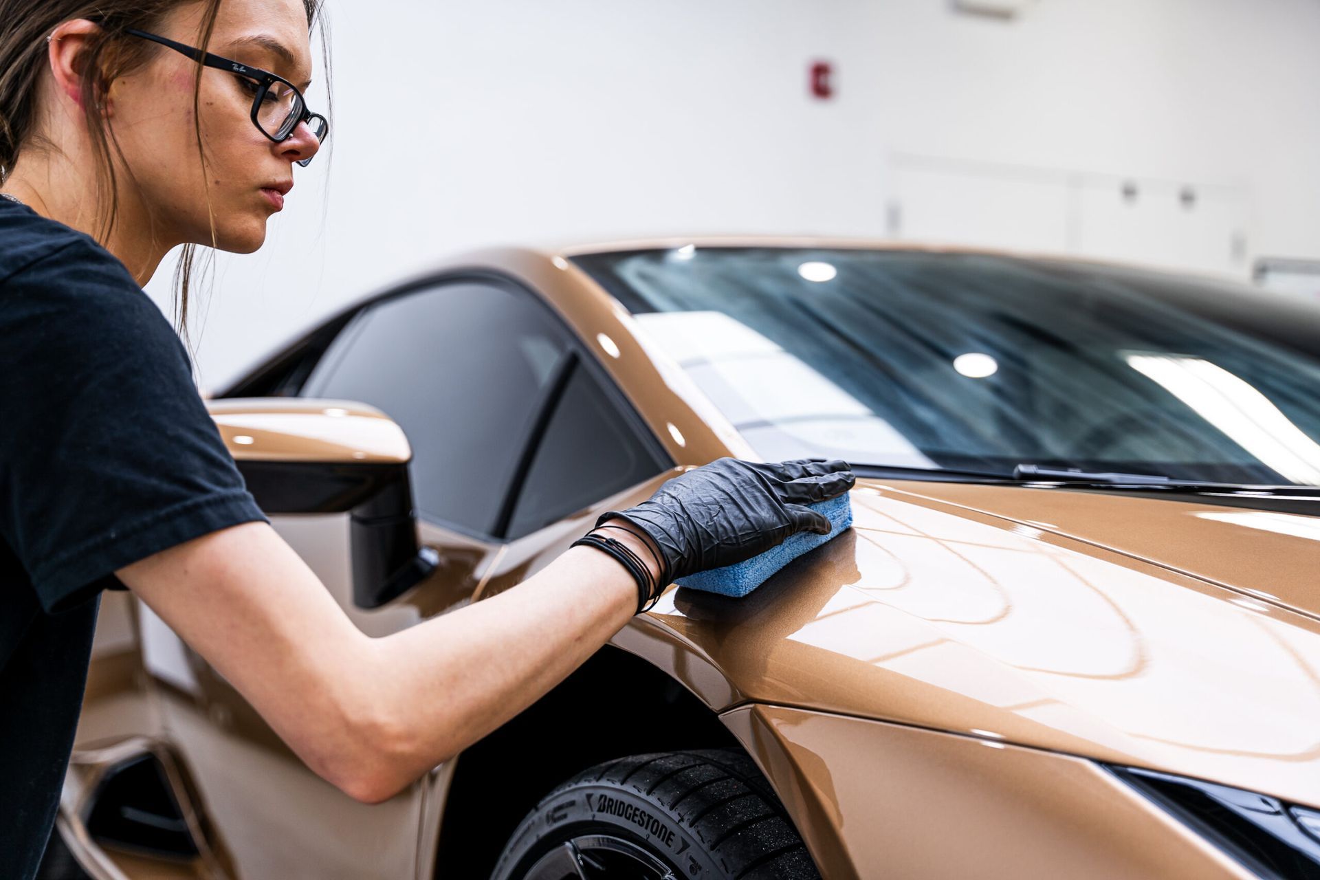 A woman is cleaning the side of a car with a cloth.