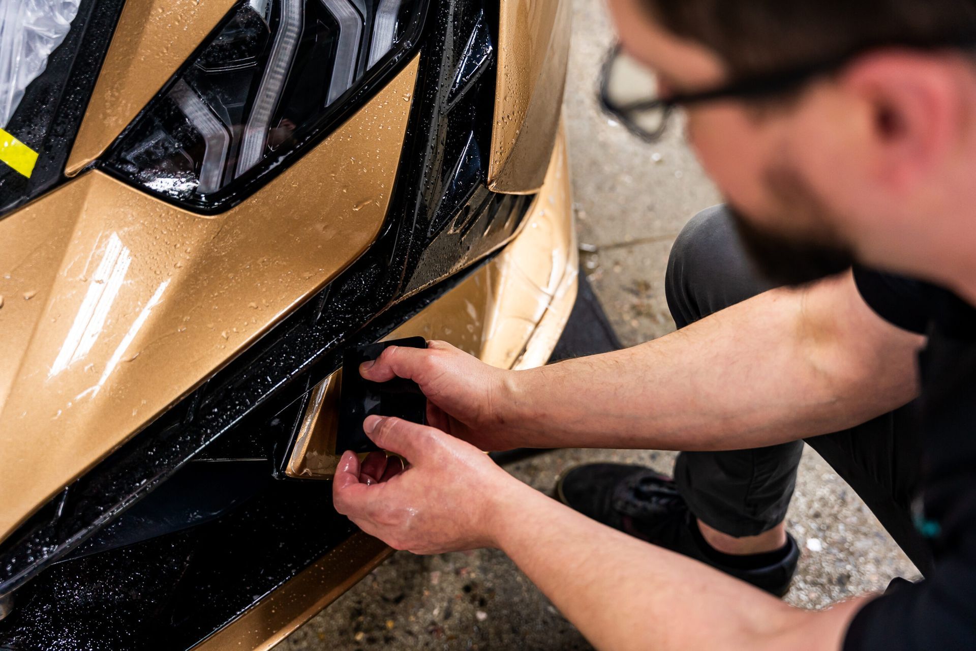 A man is applying a protective film to the front of a car.