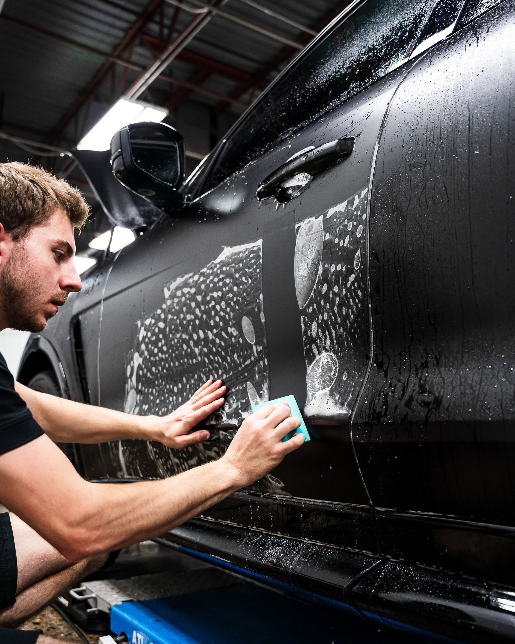 A man is cleaning the side of a black car with a sponge.