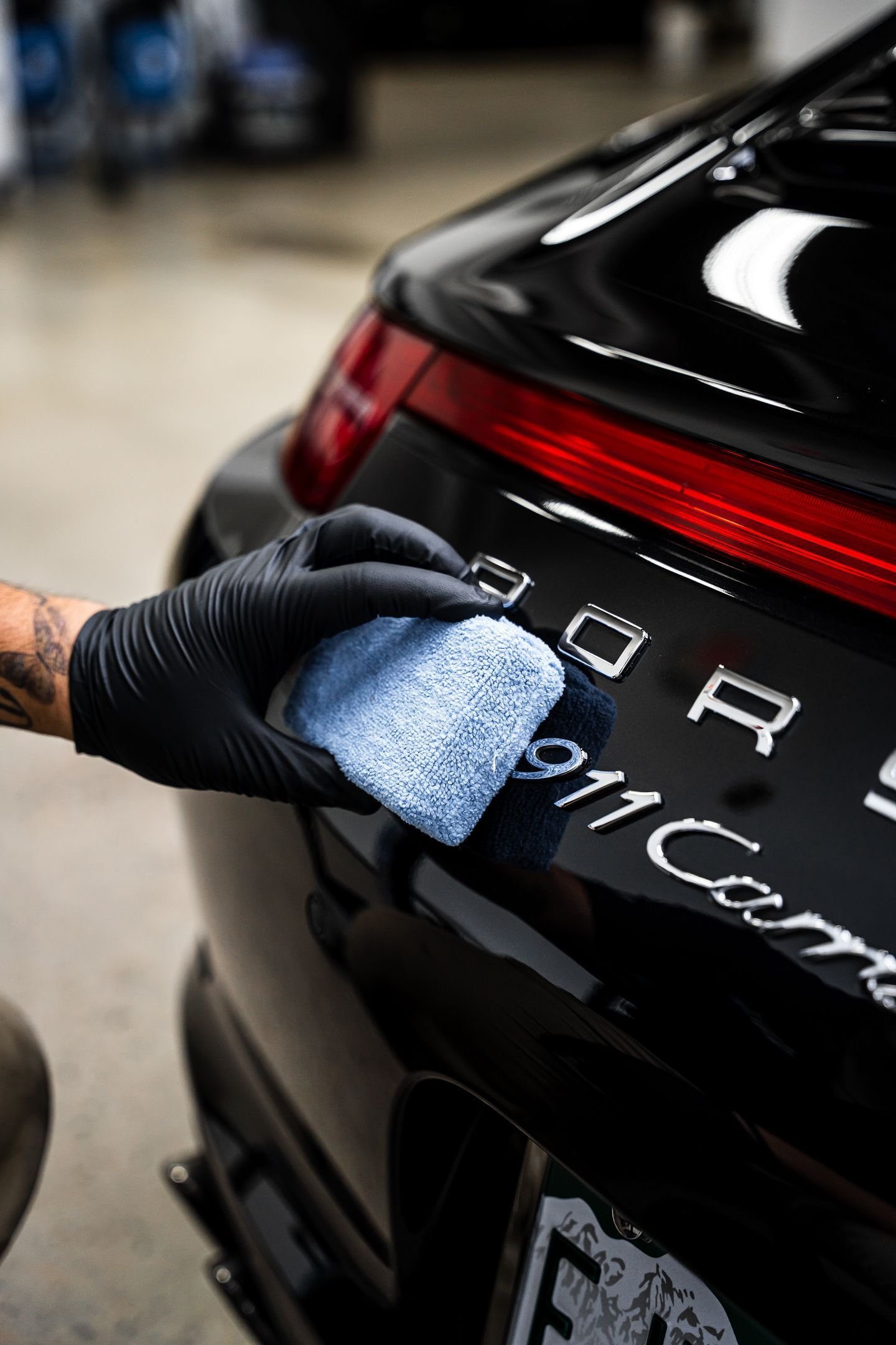A person is cleaning the back of a black porsche 911 carrera with a sponge.