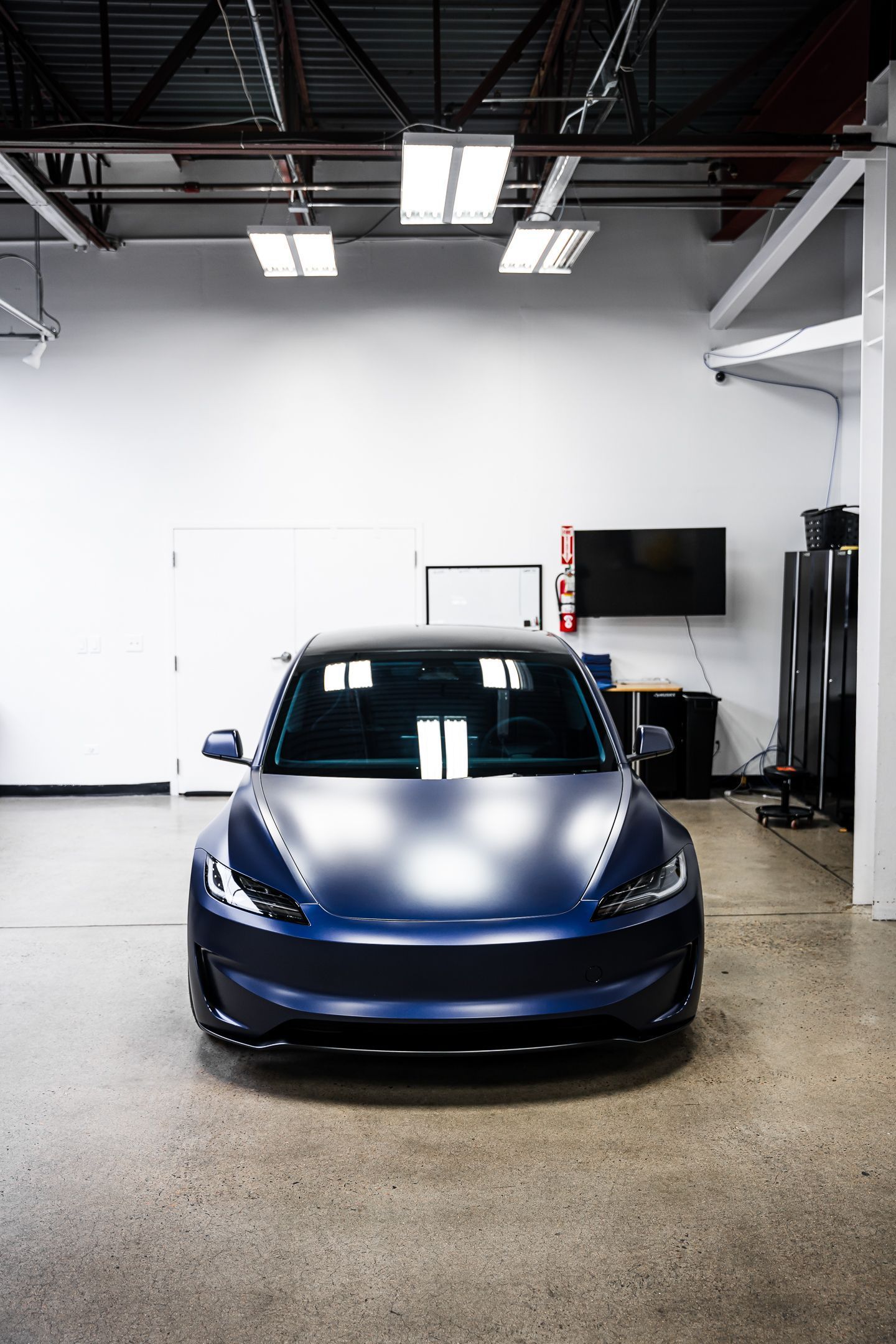 A blue tesla model 3 is parked in a garage.